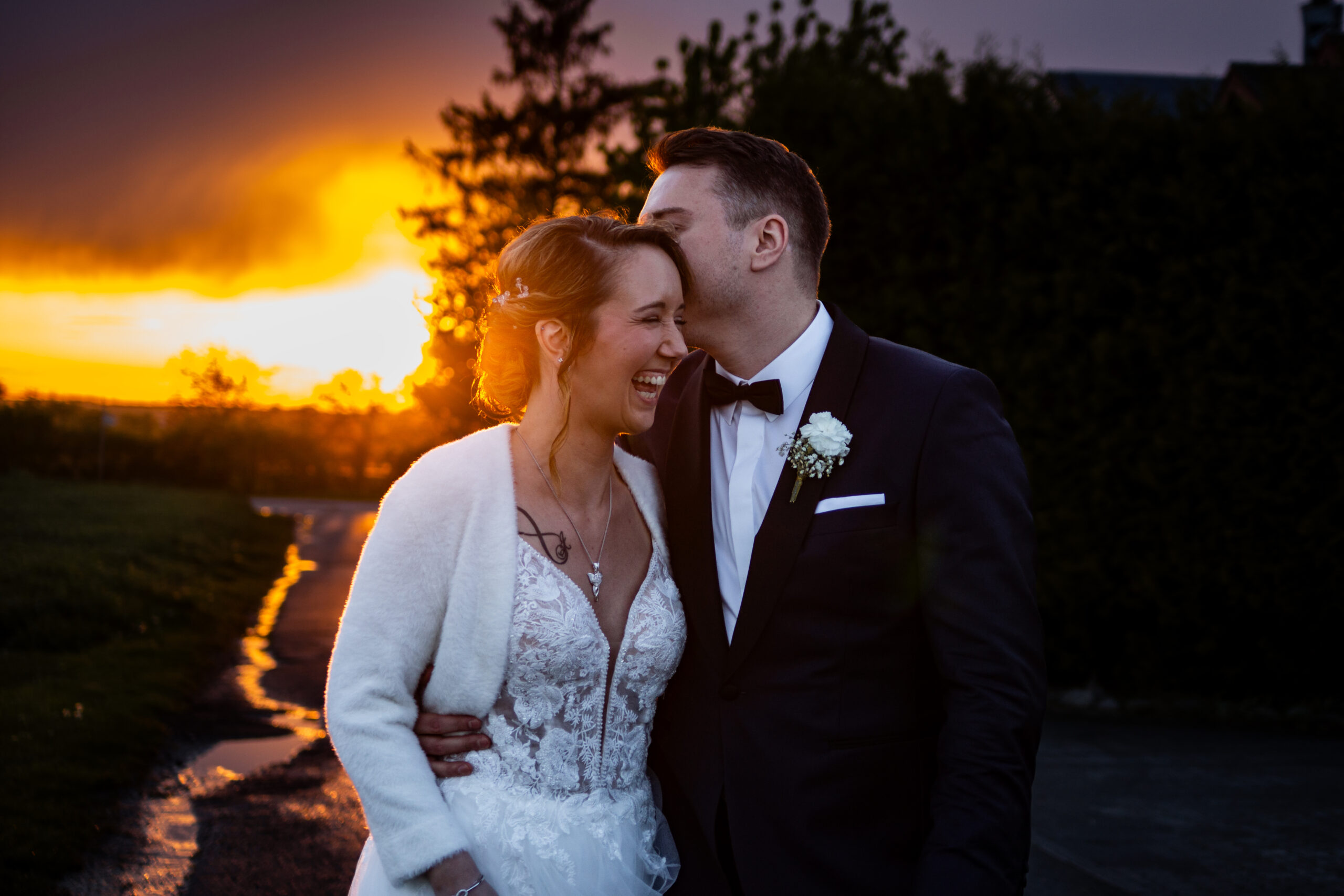 Glückliches Hochzeitspaar bei Sonnenuntergang, Bräutigam küsst Braut auf den Kopf